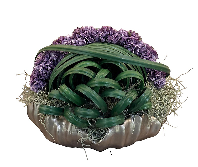Purple artificial flower with greens in clay vase